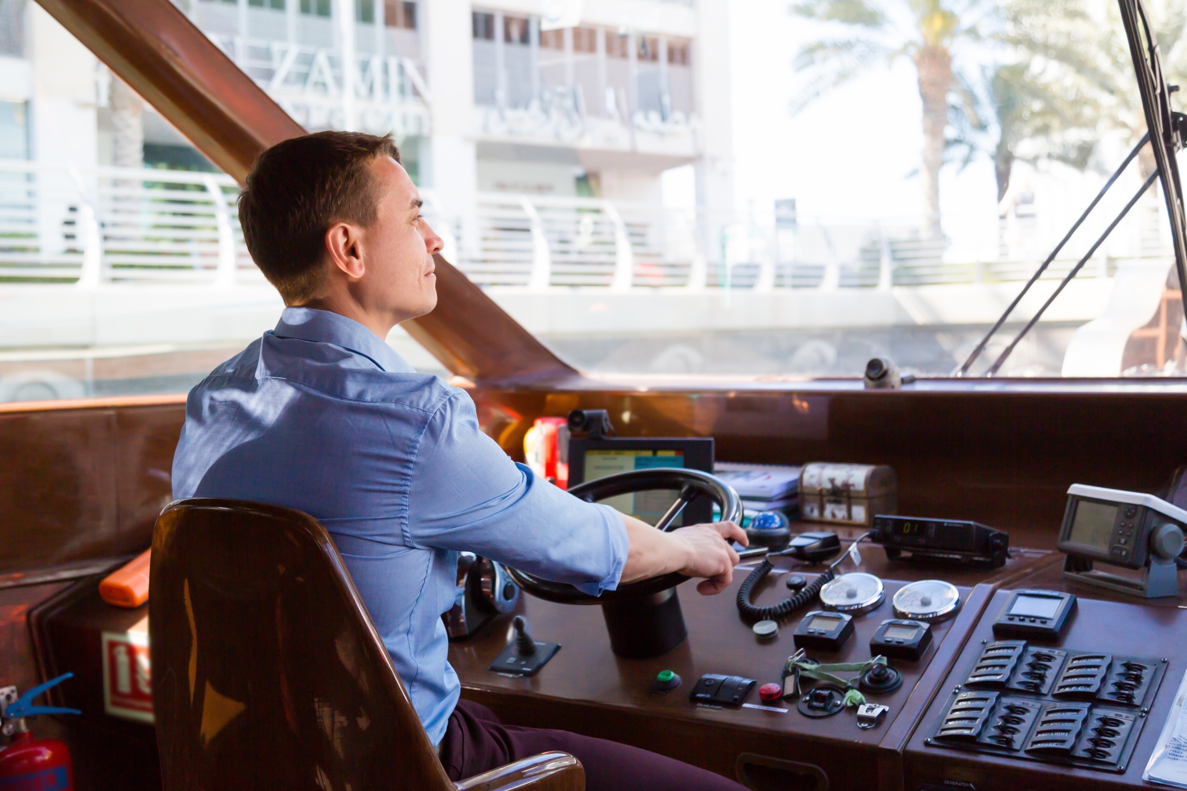 Captain at the helm of a yacht steering through a marina
