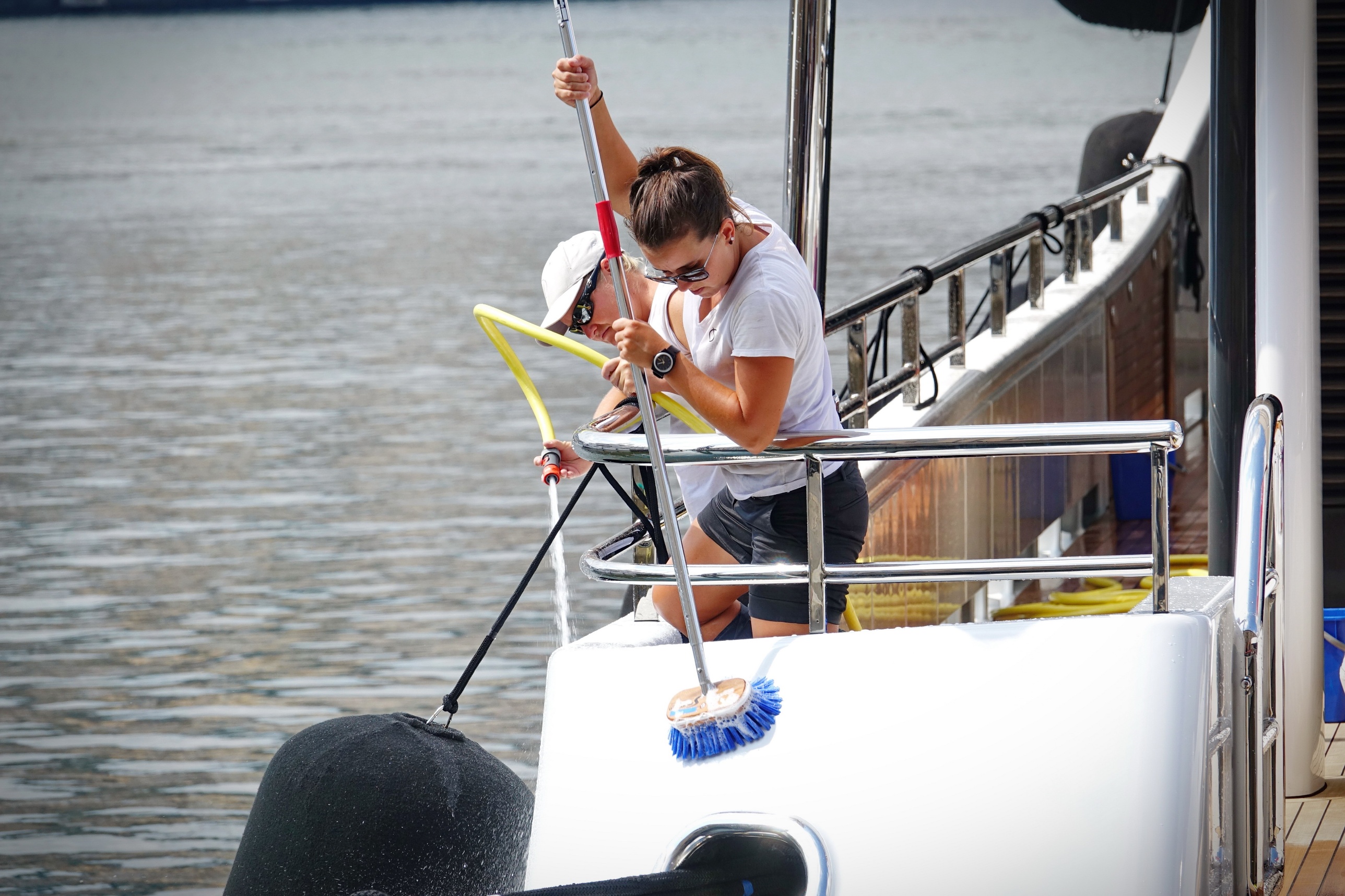 Two service crew members washing and detailing the deck of a yacht at the dock