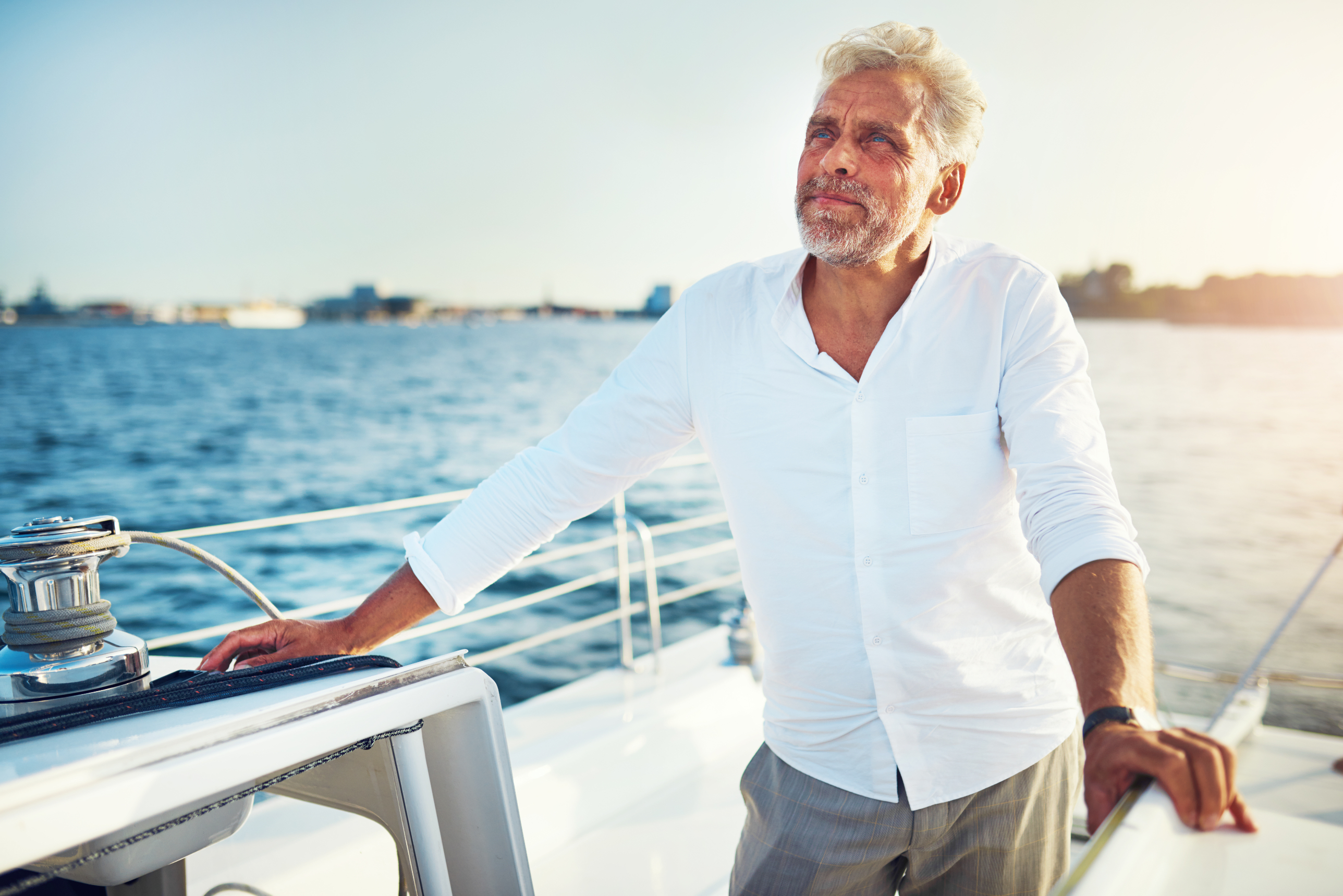 Yacht owner standing at the rail of his sailboat at golden hour, looking out over the harbor